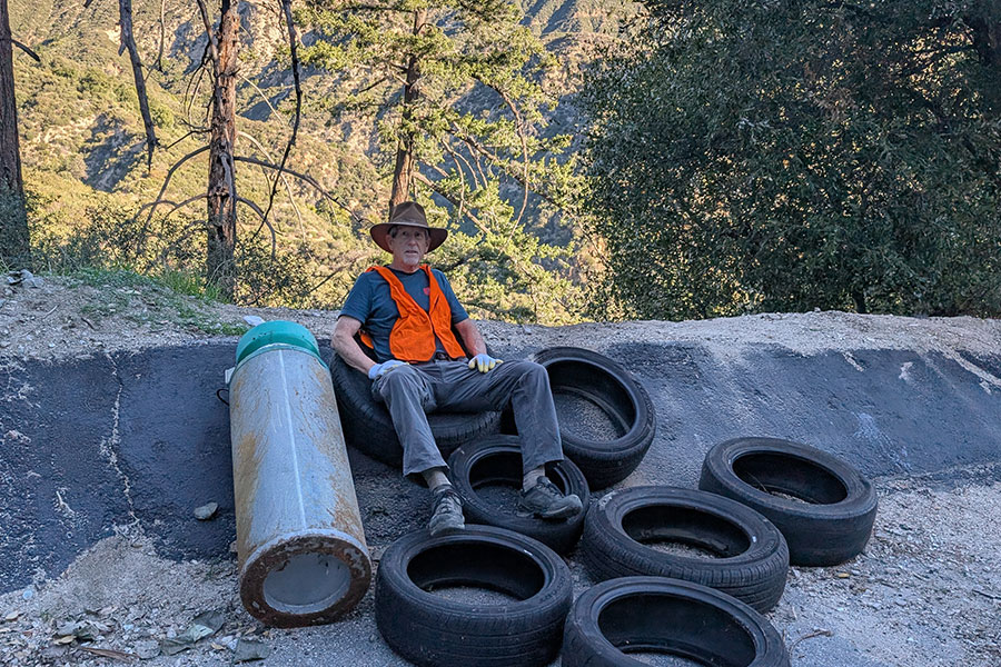 Man volunteer sitting in the forest lot with a bunch of tires and a large tank