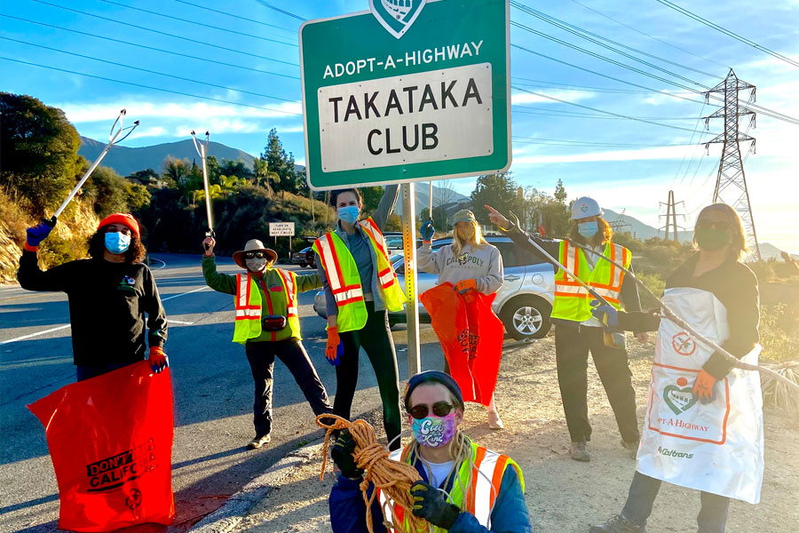 group of Takataka club volunteers in safety vests with the adopt-a-highway "Takataka club" sign